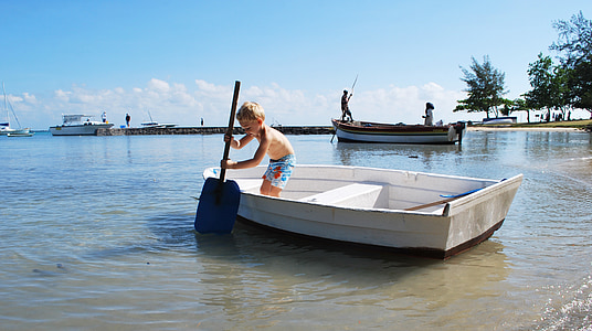 boy standing on white boat while holding blue paddle during daytime thumbnail