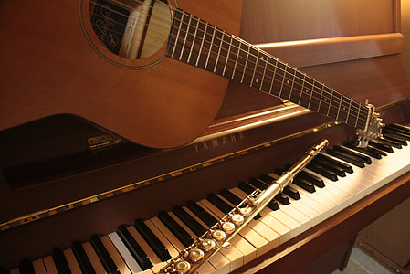 brown acoustic guitar and gray stainless steel flute on brown Yamaha upright piano thumbnail