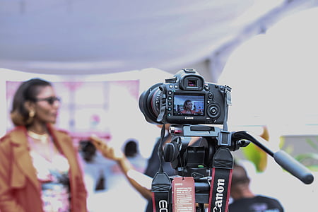 selective focus photo of Canon EOS camera pointed at woman in brown coat thumbnail