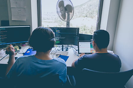 two people sitting in front of two computer monitors thumbnail
