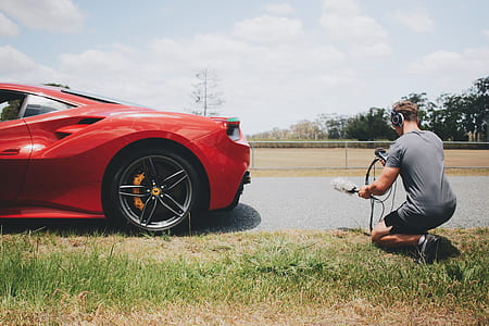 man kneeling behind red sport car thumbnail