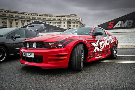 red and black Ford Mustang coupe parked beside black vehicle on concrete road thumbnail