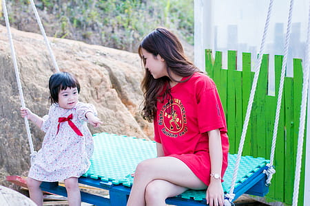 Woman Wearing Red Crew-neck Shirt Sitting on Swing Bench thumbnail