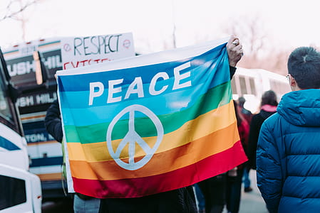 person holding rainbow flag with peace symbol in a gathering outside thumbnail