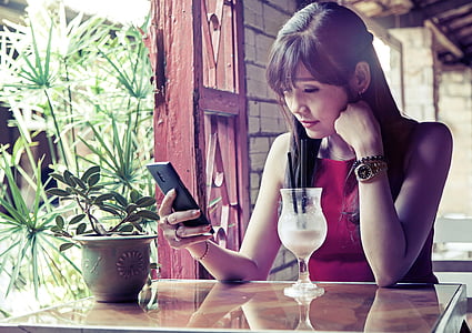 woman wearing red sleeveless top using smartphone while sitting near table thumbnail