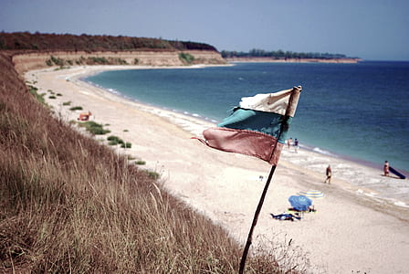 Blue Ocean Near on White Sands With White Blue and Red Flag on Shore thumbnail