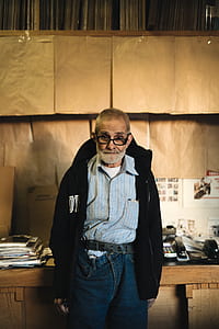 man standing in front of brown wooden desk wearing black jacket thumbnail