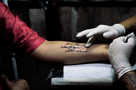 person doing tattoo quotes on person's left arm thumbnail