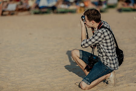 man kneeling on beige sand while taking a photo thumbnail