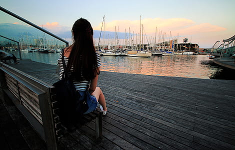 Woman in Black and White Stripe Scoop Neck Shirt Sitting on Brown Wooden Bench in Ship Dock during Daytime thumbnail