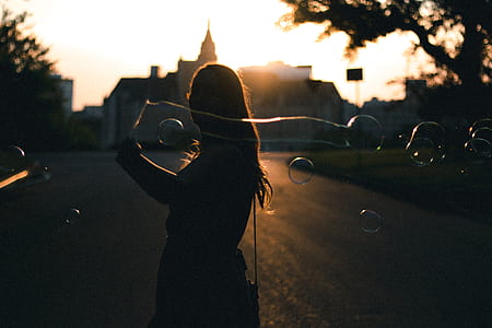 silhouette of woman creating bubbles on road during daytime thumbnail