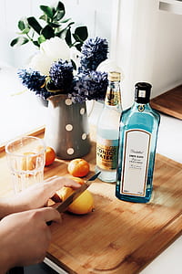 person slicing lemon near two vodka bottles and gray ceramic pot near window thumbnail