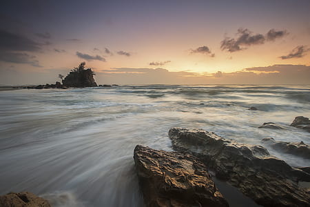 Rocks Near Body of Water Under Orange Sky during Daytime thumbnail