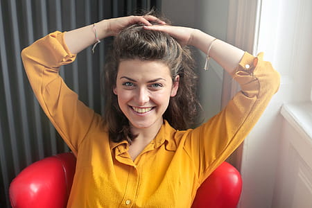 Young Woman Wearing Yellow Collared Shirt Lifting Her Hair Up With Both Hands While Sitting at Red Chair thumbnail