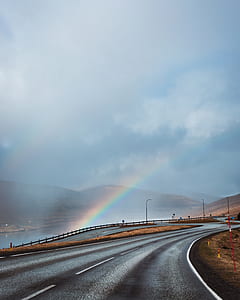 gray concrete asphalt road near brown hills under cloudy sky and rainbow at daytime thumbnail