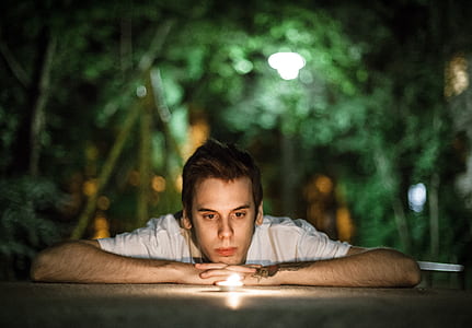 selective focus photo of man wearing white t-shirt looking closely at the lighted tealight candle thumbnail