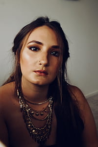 woman wearing silver-colored chain necklace sitting near white wall thumbnail