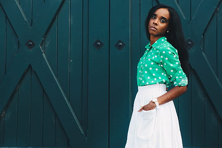 woman wearing teal and white polka-dot dress and white skirt standing near green surface thumbnail