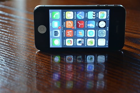 turned-on iPhone 4s displaying home screen on wood surface thumbnail