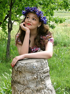 woman wearing pink floral dress and purple floral headdress resting chin on right hand thumbnail