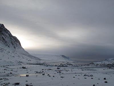 snow covered terrain with mountains under gray sky thumbnail
