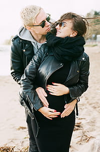 Man in Black Leather Zip Jacket Hugging Woman in Black Leather Zip Jacket and Black Pants Standing on Sand at Daytime thumbnail