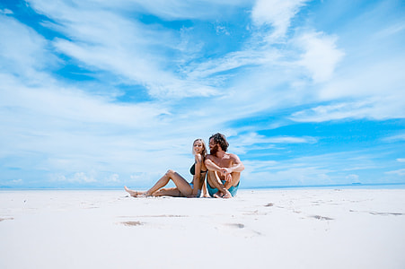 man and woman sitting on white sand shore thumbnail