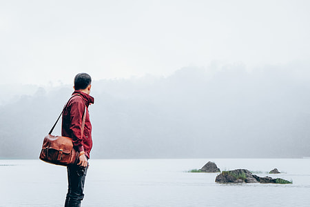 man standing near body of water and mountain during daytime thumbnail