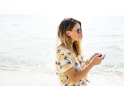 woman smiling and standing while holding phone near seashore thumbnail