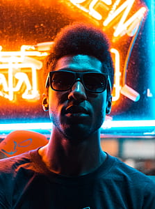 man wearing sunglasses behind neon signage thumbnail