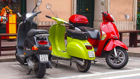 three gray, green, and red motor scooters parked beneath stores thumbnail