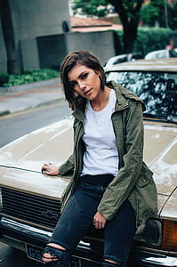 woman wearing white crew-neck shirt sitting on hood of beige Chevrolet car thumbnail