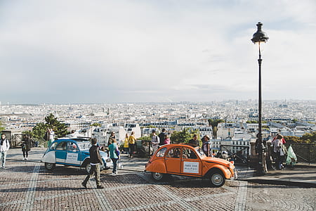 two blue and orange Volkswagen Beetle coupe on road near people standing at daytime thumbnail
