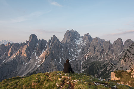 man sitting on top of a mountain facing overview of a snowy mountain thumbnail