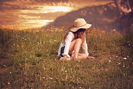 woman wearing white long-sleeved shirt and brown hat sitting on green grasses thumbnail