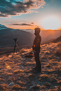 man in black top standing beside of black DSLR camera with tripod thumbnail
