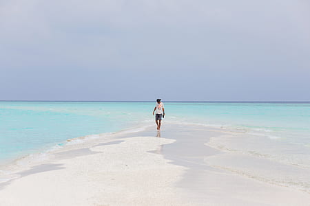 man in white crew-neck shirt walking on seashore during daytime thumbnail