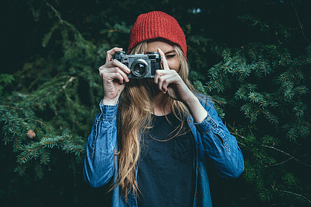 selective focus photography of woman wearing blue denim jacket holding gray film camera taking picture thumbnail
