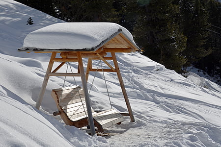 brown wooden swing bench filled with snow thumbnail