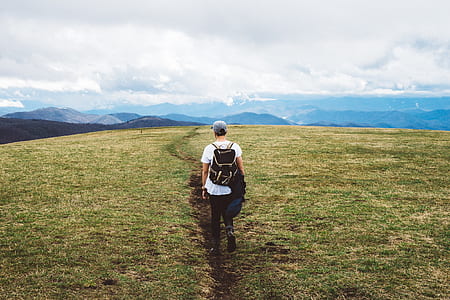 man wearing white shirt and black backpack waking on green grass field thumbnail