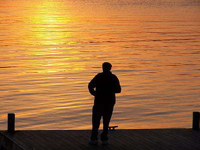 silhouette photography of person standing in front of body of water thumbnail