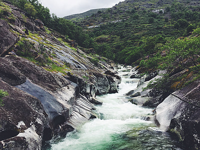 landmark photography of river beside grasses near hill under white cloudy skies thumbnail