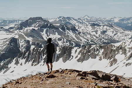 man standing facing snow coated mountain thumbnail