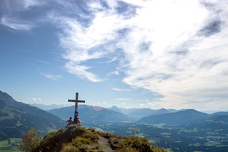 two people beside cross on mountain under white cloudy sky thumbnail
