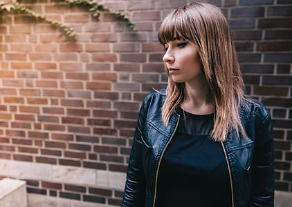 woman in black leather jacket standing near brown brick wall thumbnail