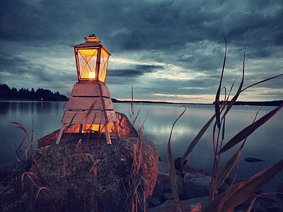 lighted brown candle lamp on gray stone overlooking still body of water under cloudy sky during daytime thumbnail