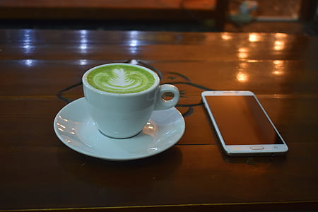 teacup filled with coffee beside Android smartphone on wooden table thumbnail