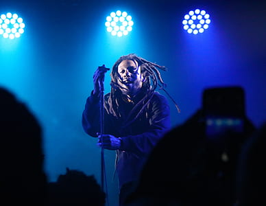 man in black pullover hoodie with dreadlocks hairstyle standing on stage thumbnail