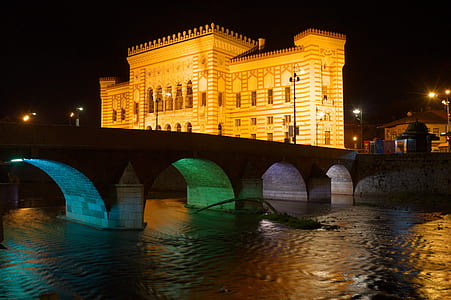 photography of gray concrete arch bridge near brown concrete building at nighttime thumbnail