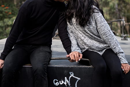 couple kissing while sitting and holding hands on black concrete bench thumbnail